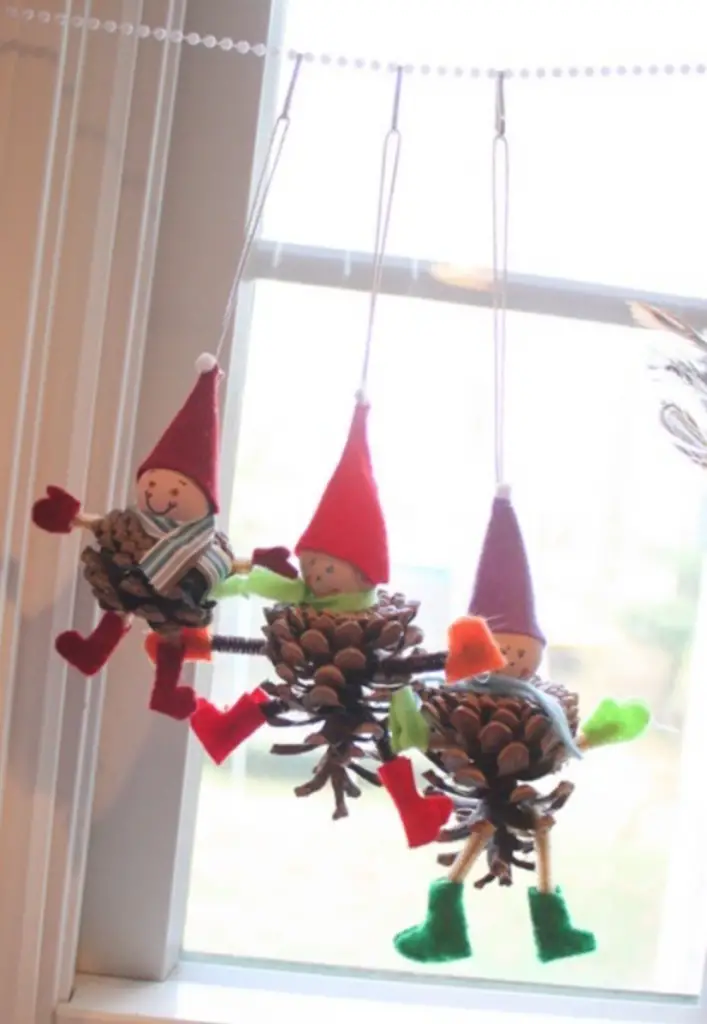 adornos navideños artesanales de elfos con piñas colgados en una ventana de Memories on Clover Lane